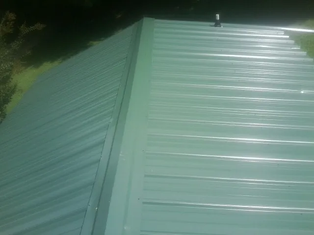 New green metal panels meeting at the ridge of a roof — Flat Roof Repair work by our crew in Pikeville